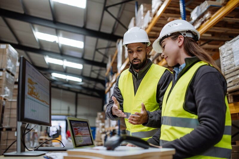 Two workers consulting with data on a computer in a warehouse