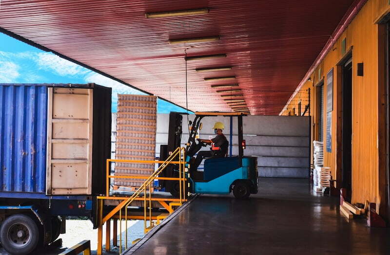 Forklift loading a shipping container at a warehouse dock