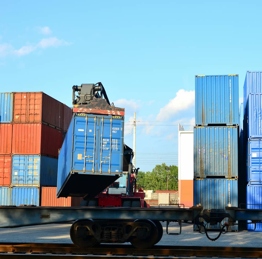 Crane unloading a shipping container onto a rail car in a transportation yard